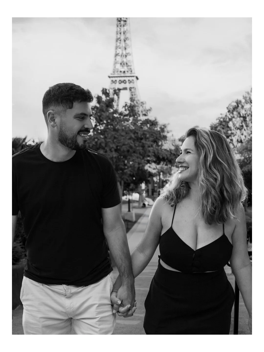 Casal caminhando de mãos dadas com a Torre Eiffel ao fundo